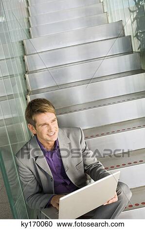 High angle view of a businessman sitting on a staircase and using a laptop View Large Photo Image Stock Image - High angle view of a businessman sitting on a staircase and using a laptop. Fotosearch