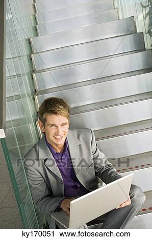 Portrait of a businessman sitting on a staircase and using a laptop View Large Photo Image Stock Image - Portrait of a businessman sitting on a staircase and using a laptop. Fotosearch