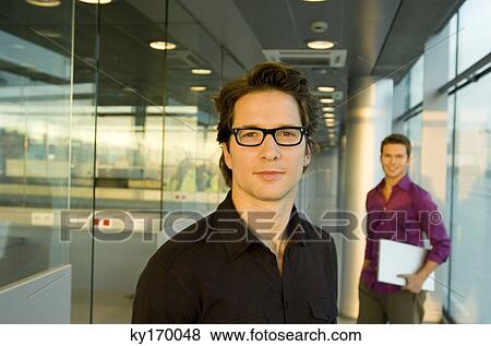 Portrait of a businessman with another businessman holding a laptop in the background View Large Photo Image Stock Photo - Portrait of a businessman with another businessman holding a laptop in the background. Fotosearch