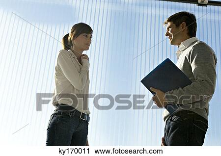 Side profile of a businessman holding a laptop and talking to a businesswoman View Large Photo Image Stock Image - Side profile of a businessman holding a laptop and talking to a businesswoman. Fotosearch