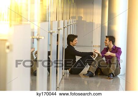 Two businessmen sitting in a corridor and talking with each other View Large Photo Image Picture - Two businessmen sitting in a corridor and talking with each other. Fotosearch