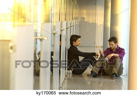 Two businessmen sitting in a corridor and talking with each other View Large Photo Image Stock Photography - Two businessmen sitting in a corridor and talking with each other. Fotosearch