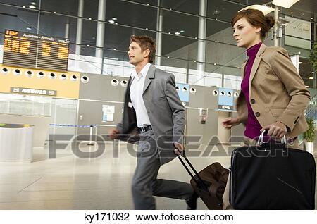 Stock Image - Businessman and a businesswoman rushing with their luggage at an airport. Fotosearch
