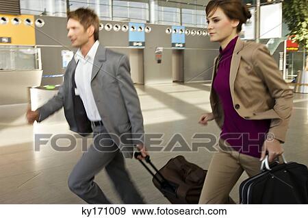 Businessman and a businesswoman rushing with their luggage at an airport View Large Photo Image Stock Photo - Businessman and a businesswoman rushing with their luggage at an airport. Fotosearch