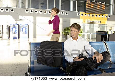 Businessman holding a mobile phone and sitting at an airport lounge View Large Photo Image Stock Image - Businessman holding a mobile phone and sitting at an airport lounge. Fotosearch