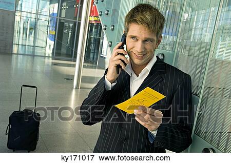 Businessman holding an airplane ticket and talking on a mobile phone at an airport View Large Photo Image Stock Photo - Businessman holding an airplane ticket and talking on a mobile phone at an airport. Fotosearch
