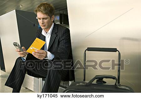Businessman sitting at an airport and operating a mobile phone View Large Photo Image Stock Photography - Businessman sitting at an airport and operating a mobile phone. Fotosearch
