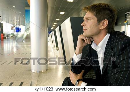 Businessman sitting at an airport lounge with his hand on his chin View Large Photo Image Stock Image - Businessman sitting at an airport lounge with his hand on his chin. Fotosearch