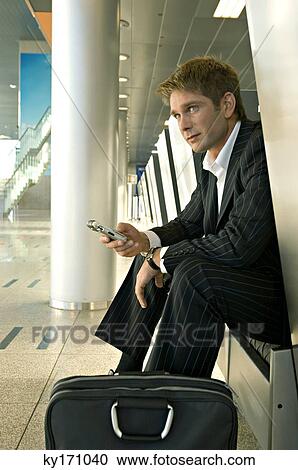 Businessman sitting at an airport lounge and operating a mobile phone View Large Photo Image Stock Image - Businessman sitting at an airport lounge and operating a mobile phone. Fotosearch