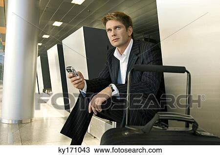 Businessman sitting at an airport lounge and holding a mobile phone View Large Photo Image Stock Image - Businessman sitting at an airport lounge and holding a mobile phone. Fotosearch