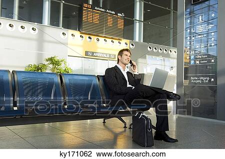 Businessman using a laptop and talking on a mobile phone at an airport lounge View Large Photo Image Stock Image - Businessman using a laptop and talking on a mobile phone at an airport lounge. Fotosearch