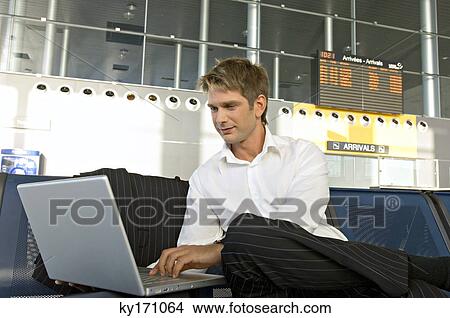 Businessman using a laptop at an airport lounge View Large Photo Image Picture - Businessman using a laptop at an airport lounge. Fotosearch