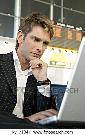 Businessman using a laptop in at an airport lounge View Large Photo Image Stock Image - Businessman using a laptop in at an airport lounge. Fotosearch
