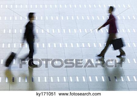 Stock Image - High angle view of two men walking at an airport lobby. Fotosearch