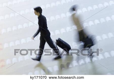 Stock Image - High angle view of two passengers walking at an airport. Fotosearch