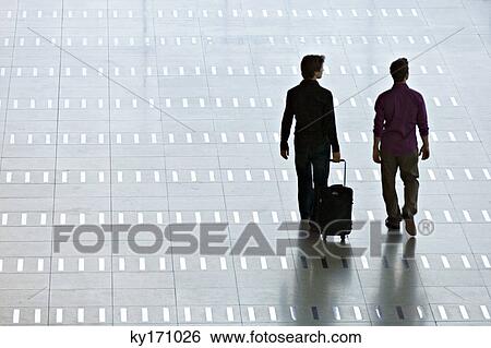 Rear view of two men walking at an airport lobby View Large Photo Image Stock Photograph - Rear view of two men walking at an airport lobby. Fotosearch