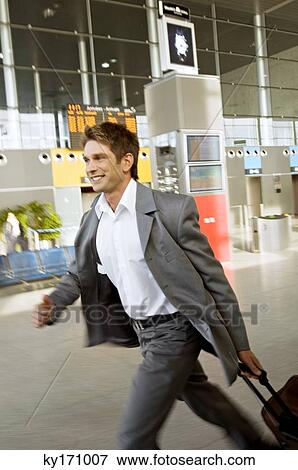 Stock Photo - Side profile of a businessman rushing with his luggage at an airport. Fotosearch