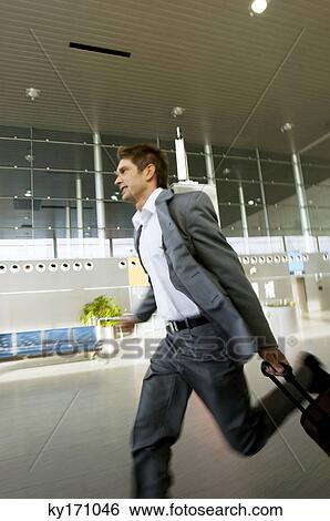 Side profile of a businessman rushing with his luggage at an airport View Large Photo Image Stock Photograph - Side profile of a businessman rushing with his luggage at an airport. Fotosearch