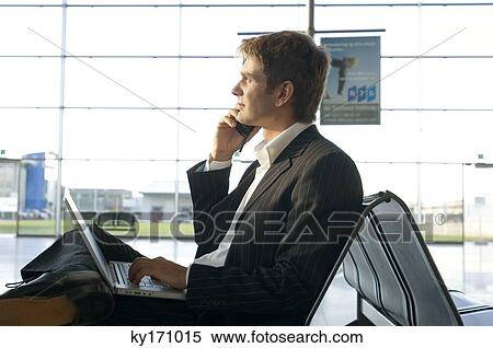 Side profile of a businessman using a laptop and talking on a mobile phone at an airport lounge View Large Photo Image Stock Photography - Side profile of a businessman using a laptop and talking on a mobile phone at an airport lounge. Fotosearch