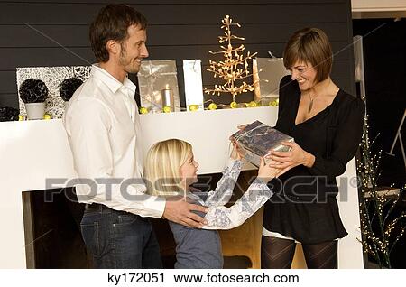 Girl giving a Christmas present to her mother with father standing behind her View Large Photo Image Stock Image - Girl giving a Christmas present to her mother with father standing behind her. Fotosearch