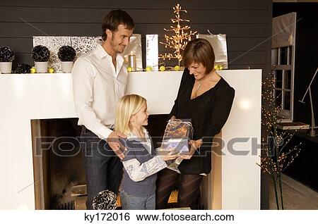 Stock Photograph - Girl giving a Christmas present to her mother with father standing behind her. Fotosearch