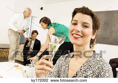 Mid adult woman holding a wine glass with three people in the background View Large Photo Image Stock Image - Mid adult woman holding a wine glass with three people in the background. Fotosearch