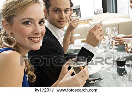 Portrait of a young couple holding glasses of champagne at a dinner party with their friends View Large Photo Image Stock Photo - Portrait of a young couple holding glasses of champagne at a dinner party with their friends. Fotosearch