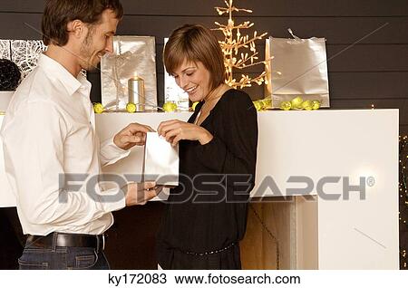 Stock Image - Side profile of a mid adult man giving a Christmas present to his wife. Fotosearch