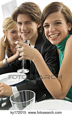 Stock Photography - Two young women with a teenage boy at a dinner party. Fotosearch