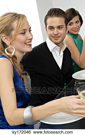 Stock Photograph - Young man with two young women at a dinner party. Fotosearch