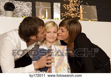 Stock Image - Young woman and a mid adult man kissing their daughter. Fotosearch