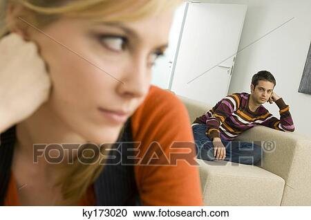 Close-up of a young woman thinking with a young man sitting on a couch in the background View Large Photo Image Stock Image - Close-up of a young woman thinking with a young man sitting on a couch in the background. Fotosearch