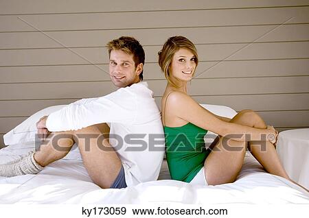 Portrait of a couple sitting back to back on the bed View Large Photo Image Stock Photo - Portrait of a couple sitting back to back on the bed. Fotosearch