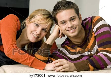Stock Image - Portrait of a young couple lying on a couch and smiling. Fotosearch