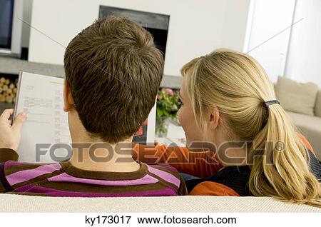Rear view of a young couple reading a magazine View Large Photo Image Stock Photo - Rear view of a young couple reading a magazine. Fotosearch