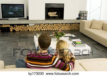 Rear view of a young couple sitting on a couch and watching television View Large Photo Image Stock Image - Rear view of a young couple sitting on a couch and watching television. Fotosearch