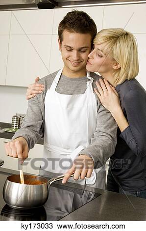 Young man cooking food and a young woman kissing him from behind in the kitchen View Large Photo Image Stock Image - Young man cooking food and a young woman kissing him from behind in the kitchen. Fotosearch