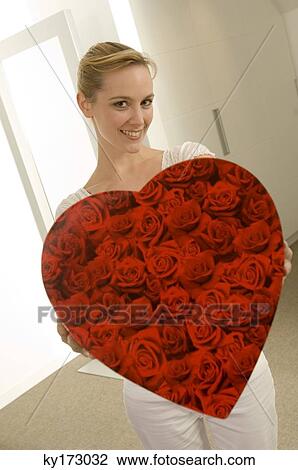 Young woman holding a heart shape gift and smiling View Large Photo Image Stock Image - Young woman holding a heart shape gift and smiling. Fotosearch