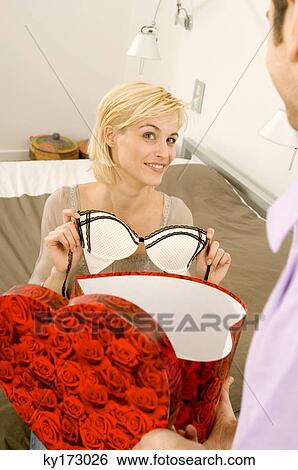 Young woman sitting in front of a young man and holding a bra View Large Photo Image Stock Photograph - Young woman sitting in front of a young man and holding a bra. Fotosearch