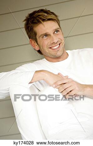 Stock Photo - Mid adult man sitting on a couch and smiling. Fotosearch