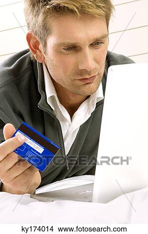 Picture - Mid adult man working on a laptop and holding a credit card. Fotosearch