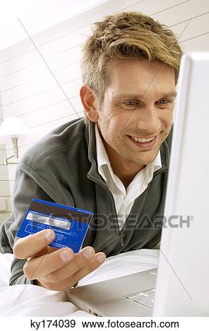Mid adult man working on a laptop and holding a credit card View Large Photo Image Stock Photo - Mid adult man working on a laptop and holding a credit card. Fotosearch