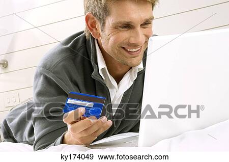 Mid adult man working on a laptop and holding a credit card View Large Photo Image Stock Photo - Mid adult man working on a laptop and holding a credit card. Fotosearch
