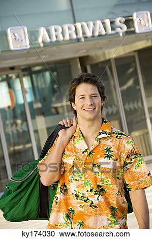 Stock Image - Portrait of a mid adult man carrying his luggage at an airport. Fotosearch