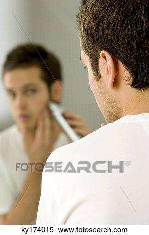 Rear view of a young man shaving with an electric razor View Large Photo Image Stock Photography - Rear view of a young man shaving with an electric razor. Fotosearch