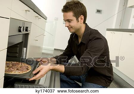Young man putting a tray of pizza into an oven and smiling View Large Photo Image Stock Photo - Young man putting a tray of pizza into an oven and smiling. Fotosearch
