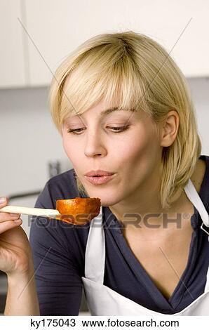 Stock Image - Close-up of a young woman blowing tomato sauce on a wooden spoon. Fotosearch