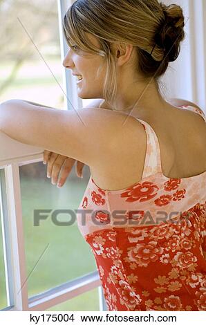 Picture - Close-up of a young woman looking through a window and smiling. Fotosearch