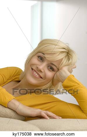 Stock Photo - Portrait of a young woman lying on a couch and smiling. Fotosearch