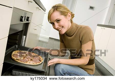 Portrait of a young woman putting a tray of pizza into an oven View Large Photo Image Picture - Portrait of a young woman putting a tray of pizza into an oven. Fotosearch